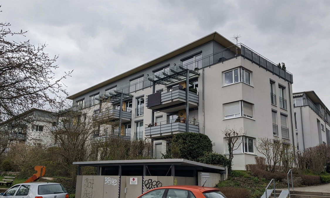 Ansicht der Fassade und der Balkon eines Mehrfamilienhauses von der Straße aus. An einem Balkon hängt ein Photovoltaikmodul
